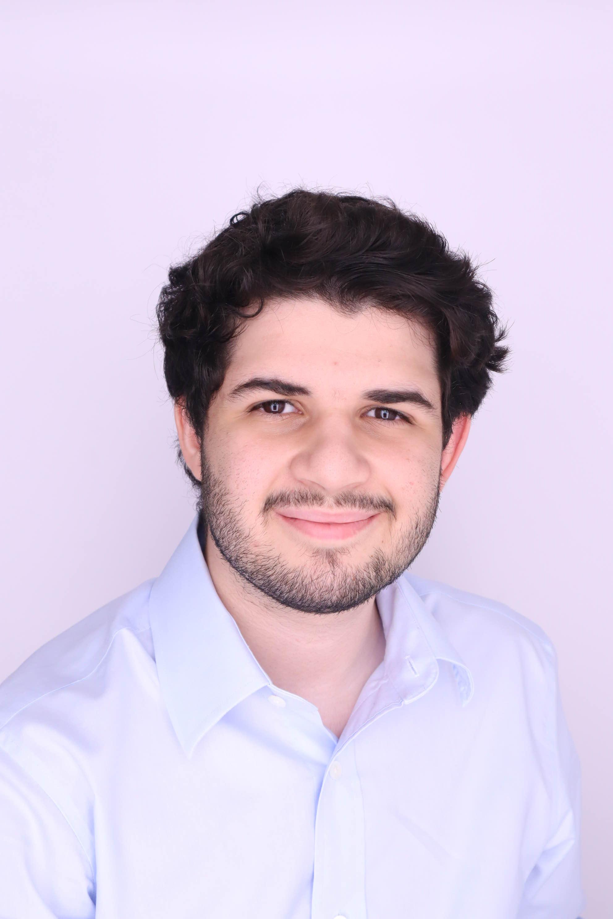 A picture of David Rodriguez wearing a light-blue button-up shirt. The background is white.